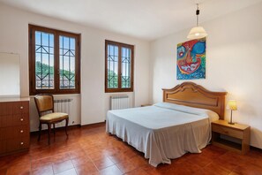 Ein Schlafzimmer mit Bett, Stuhl, Schminktisch, Heizkörper, Fenster und einem Bild an der Wand.