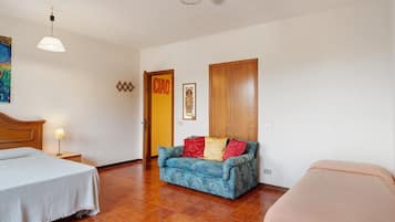 A hotel room with two beds, a sofa, a ceiling fan, a painting, and a door marked 'CIAO'.