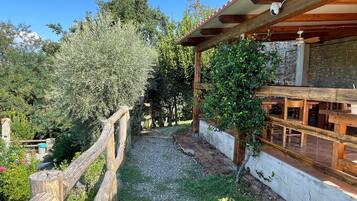 Una pergola in legno con un muro in pietra e un vialetto sterrato che conduce a un'area relax con panche di legno.