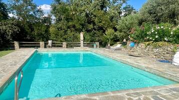 A rectangular swimming pool with stone tiles, surrounded by a stone wall and a wooden fence.