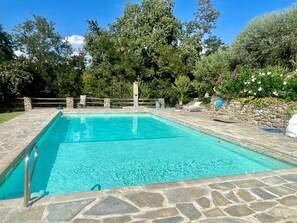 Una piscina rectangular con baldosas de piedra, rodeada por un muro de piedra y una valla de madera.