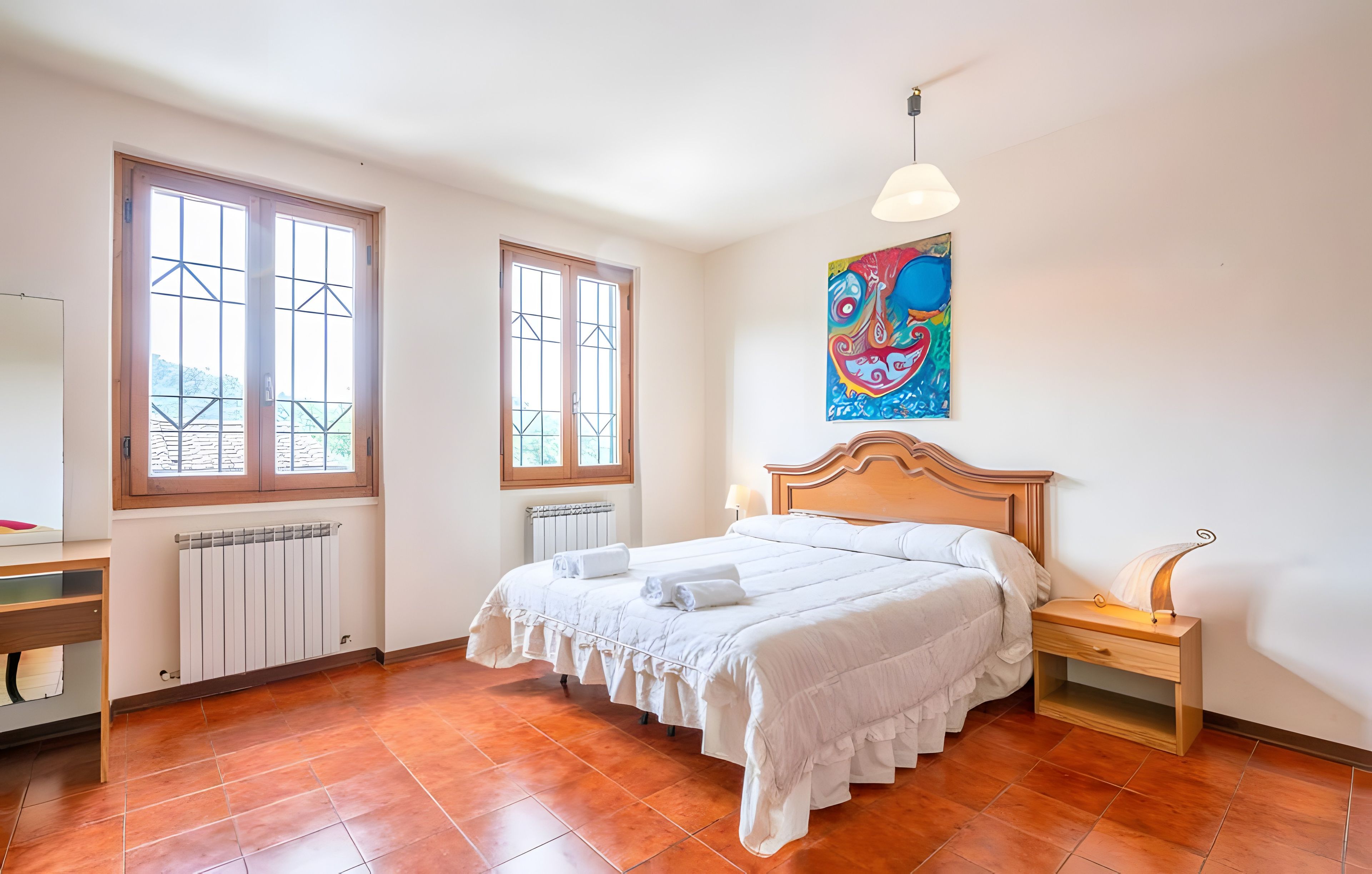 Een slaapkamer met een bed, een nachtkastje, een lamp, een radiator en een raam met uitzicht.