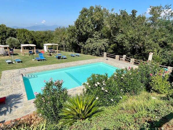 A swimming pool with lounge chairs and a stone deck, surrounded by greenery and a stone fence.