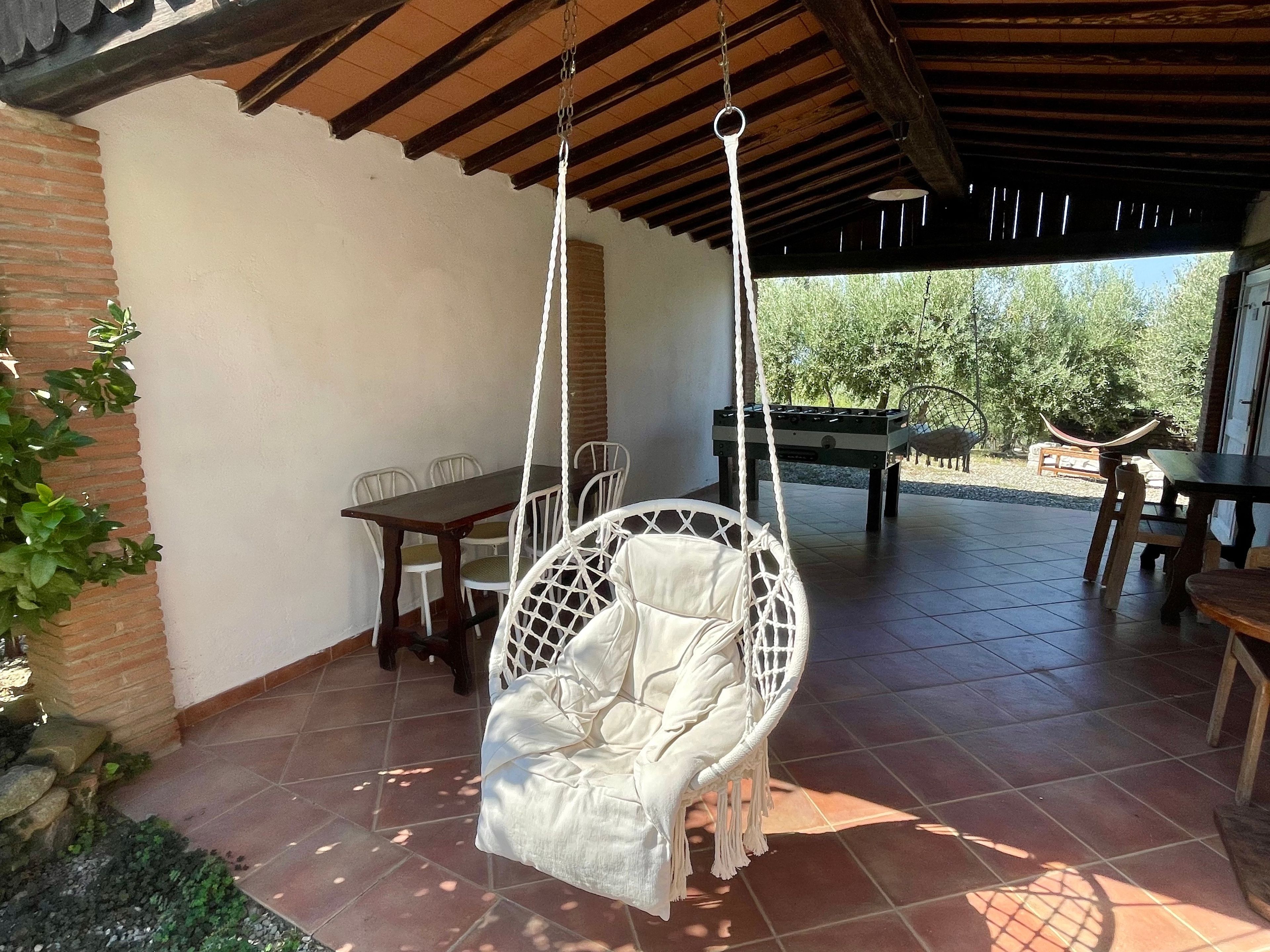 Een overdekt terras met een hangstoel, een tafel en stoelen.