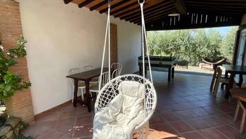 Een overdekt terras met een hangstoel, een tafel en stoelen.