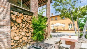Un patio con una parrilla de piedra, leña apilada y un muro de ladrillo.
