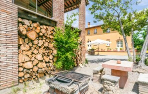 En terrasse med en sten grill, stablet brænde og en murstensvæg.