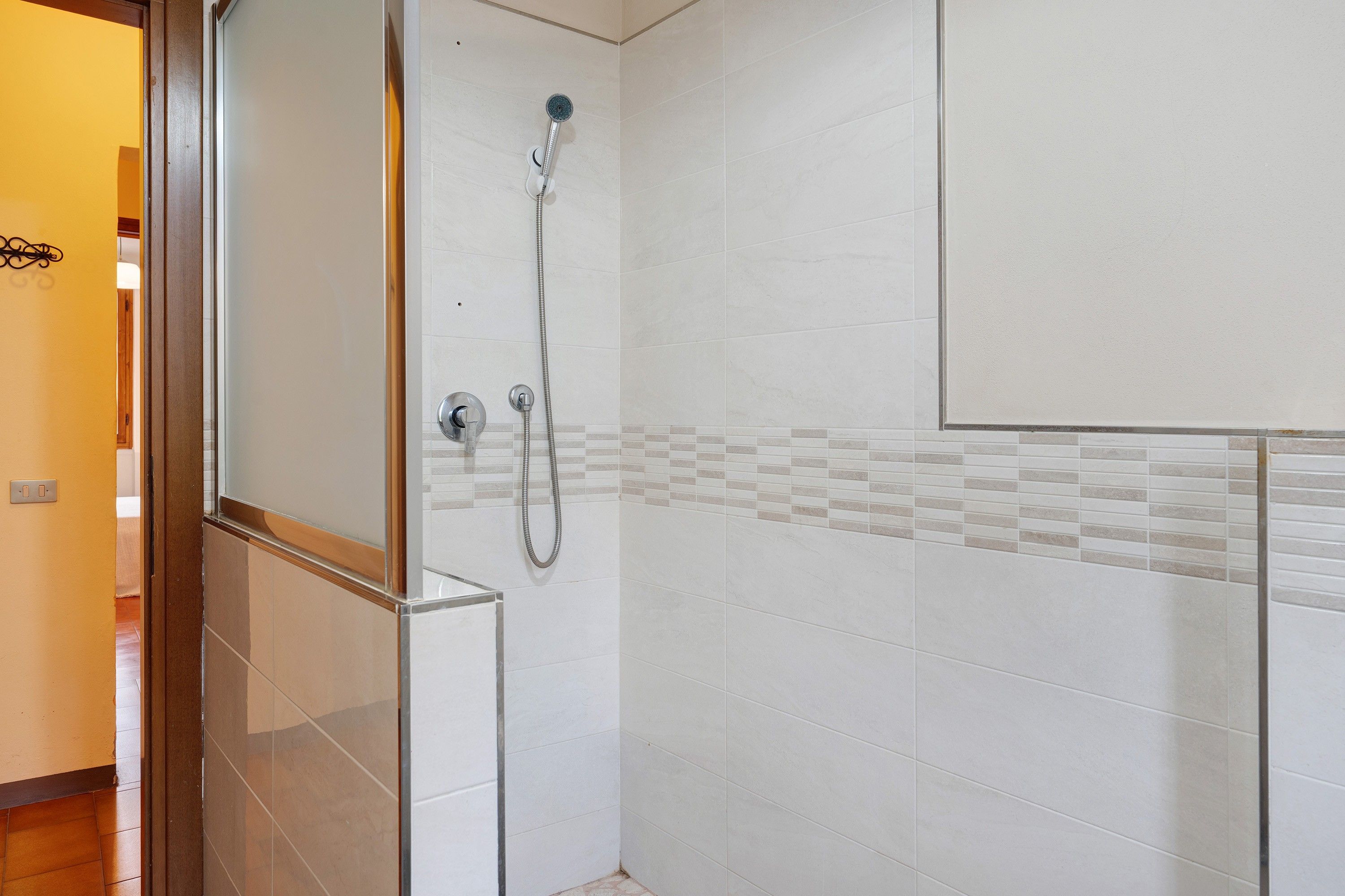 Un bagno con doccia, pareti piastrellate e stipite della porta visibile.