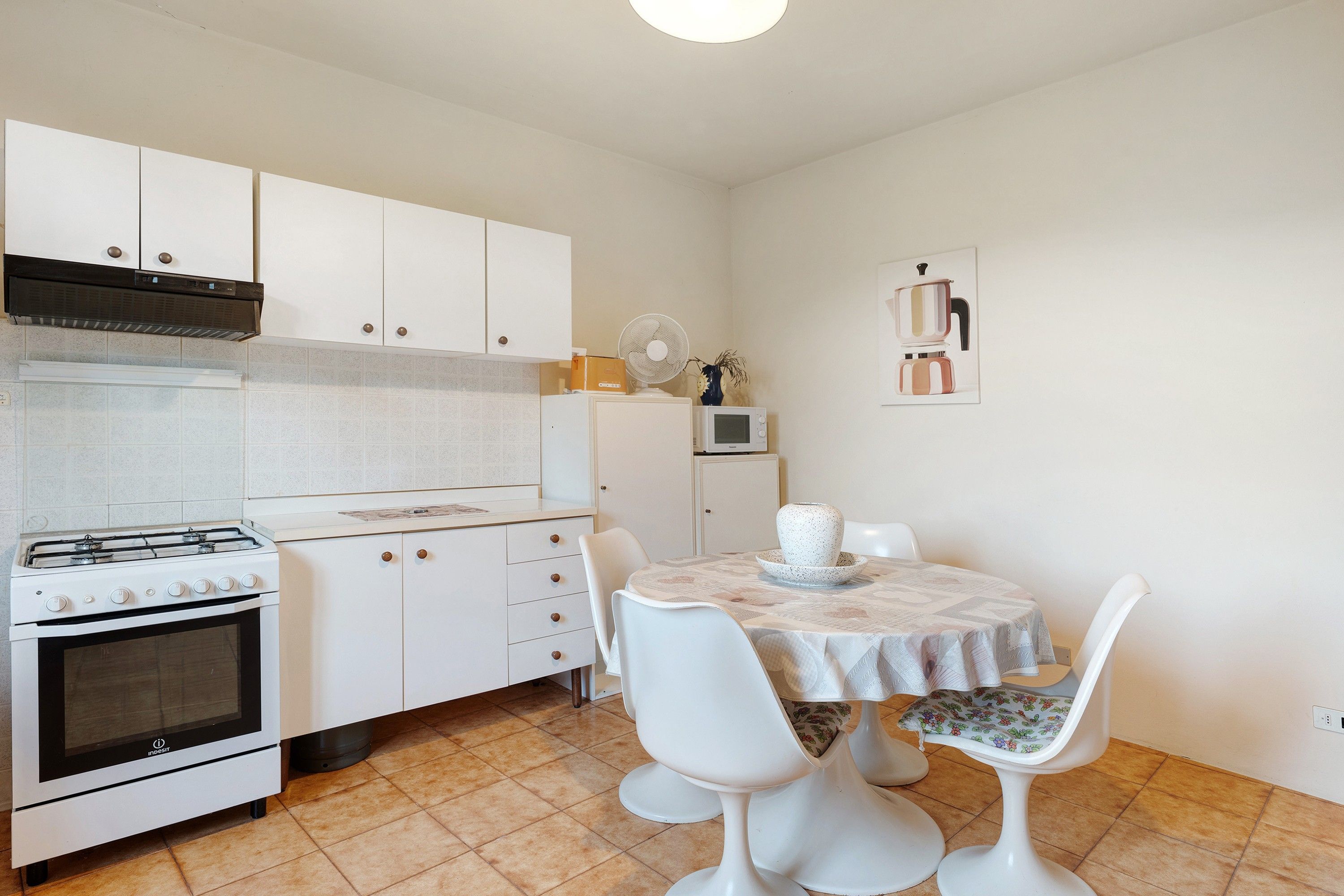 Een compacte keuken met witte kasten, een gasfornuis, een magnetron en een eethoek met een tafel en stoelen.