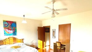 Un dormitorio con cama, escritorio, silla, ventilador de techo y un cuadro en la pared.