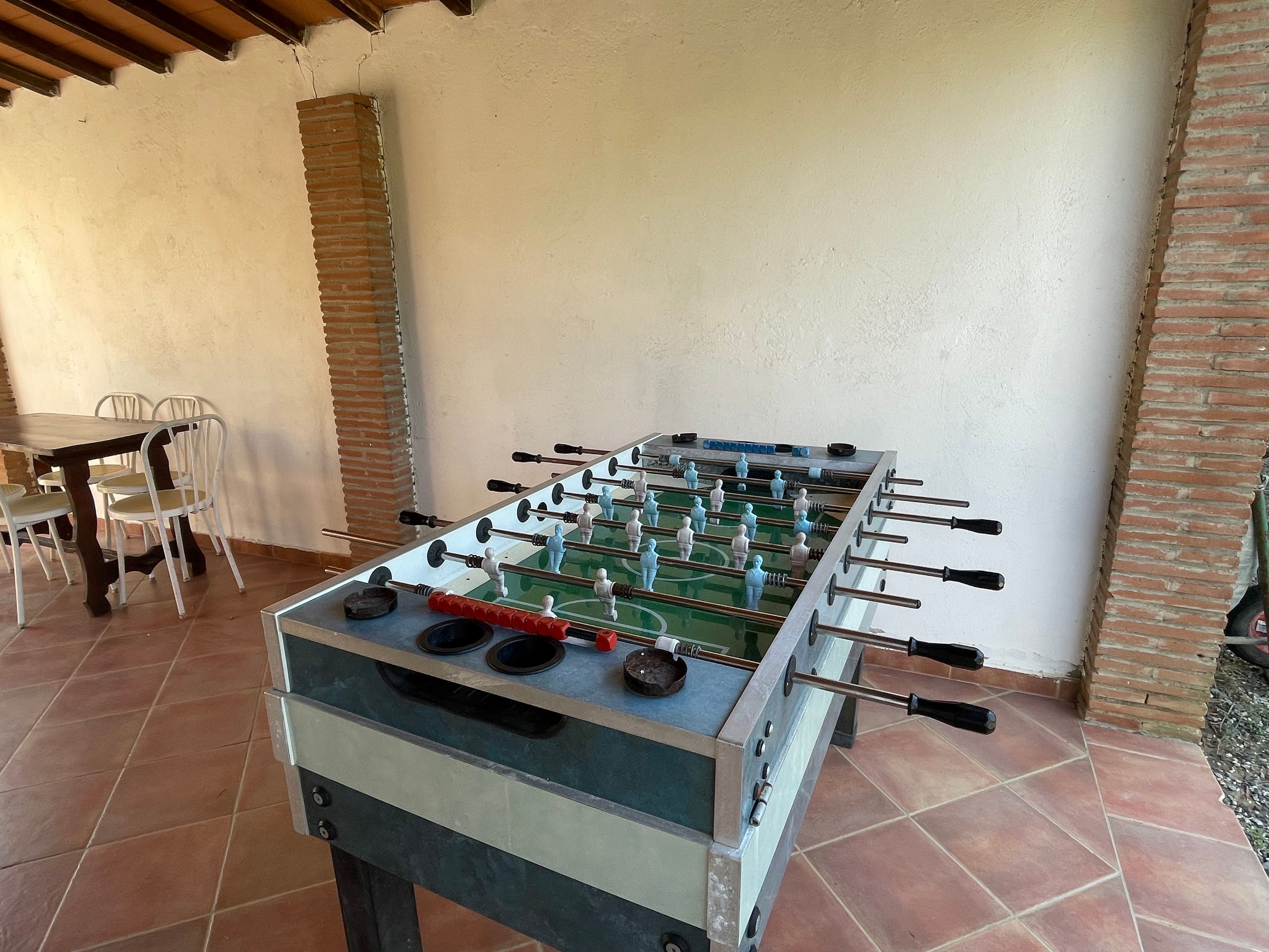 Une table de baby-foot dans une pièce dont le sol est carrelé, qui possède un mur en briques et un plafond blanc.