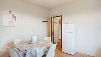 A dining area with a table set for two, a white refrigerator, and a door with a sign.