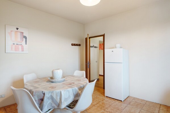 A dining area with a table set for two, a white refrigerator, and a door with a sign.