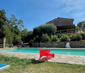 En swimmingpool med en stenvæg og en rød stol i forgrunden.