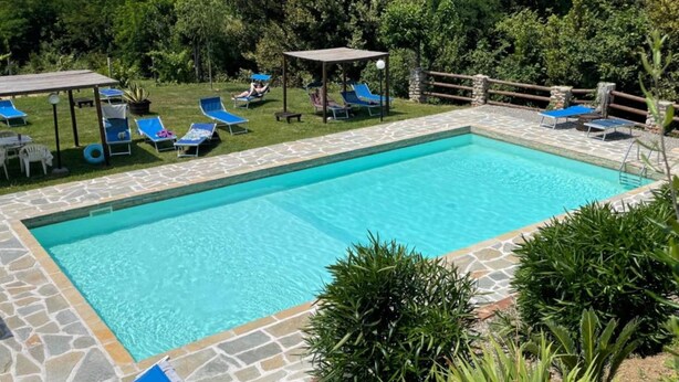Piscina rectangular con borde de piedra, rodeada de sillas de descanso y una pérgola.