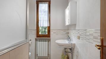 Ein Badezimmer mit Toilette, Waschbecken, einem Fenster mit Vorhang, einem Heizkörper und einem Mülleimer.