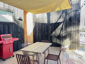 Une terrasse extérieure avec une table et des chaises en bois, un barbecue rouge et un auvent jaune.