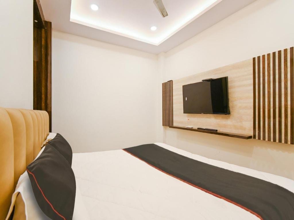 Habitació d'hotel amb un llit, una televisió penjada a la paret i una lluminària al sostre.