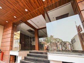 Entrada de hotel com teto de madeira, portas de vidro e escadaria que leva para o interior.