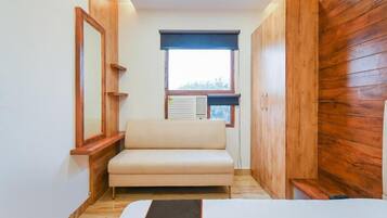 A room with a sofa, a window with blinds, a radiator, and wooden paneling on the walls.