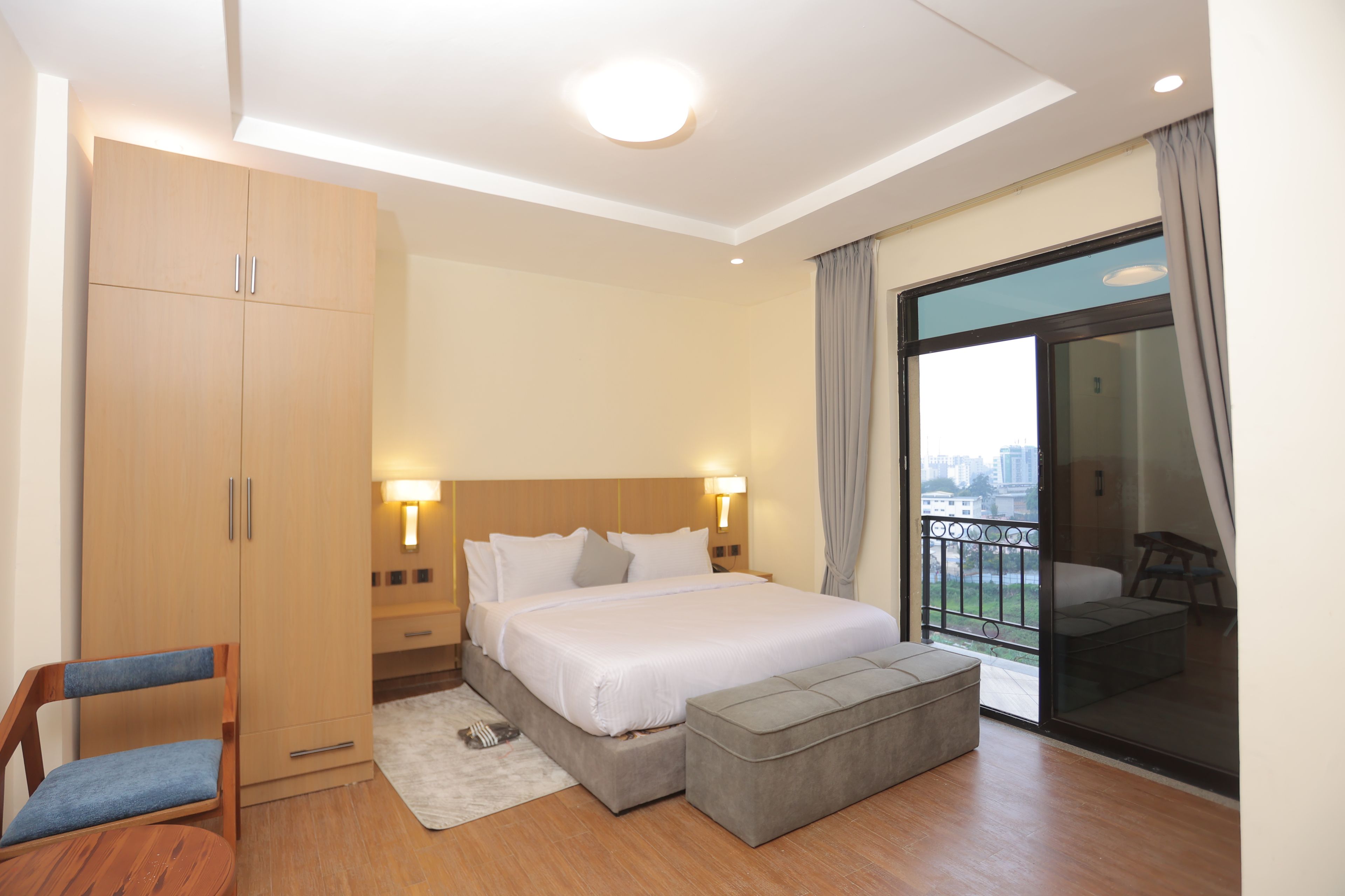Ein Hotelzimmer mit einem Bett, einem Kleiderschrank, einem Sessel und einem kleinen Hocker, sowie einem Balkon mit Aussicht.