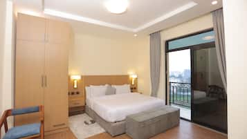 Una camera d'albergo con un letto, un armadio, una sedia, un poggiapiedi e un balcone con vista.