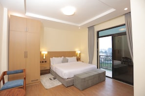 A hotel room with a bed, a wardrobe, a chair, a small ottoman, and a balcony with a view.