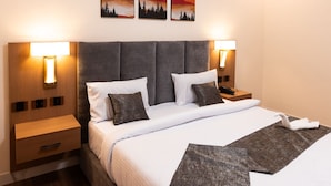 Habitación de hotel con una cama grande, dos mesitas de noche, una mesita auxiliar de madera y lámparas fijadas a la pared.
