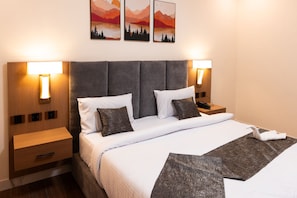 A hotel room with a large bed, two bedside tables, a wooden nightstand, and wall-mounted lamps. - Di Napoli Hotel (Addis Ababa)