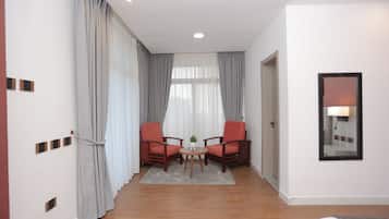 Una camera d'albergo con due sedie in legno, un tavolino rotondo, un tappeto grigio e uno specchio a parete.