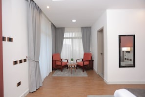 A hotel room with two wooden chairs, a small round table, a grey rug, and a mirror on the wall.