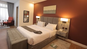 Habitación de hotel con una cama grande, una mesita de noche con teléfono, una silla, un espejo y un cuadro en la pared.