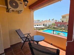 A balcony with a pool view, a chair, a table, and an air conditioning unit. - Amber Apartment by Staycare (Rota)