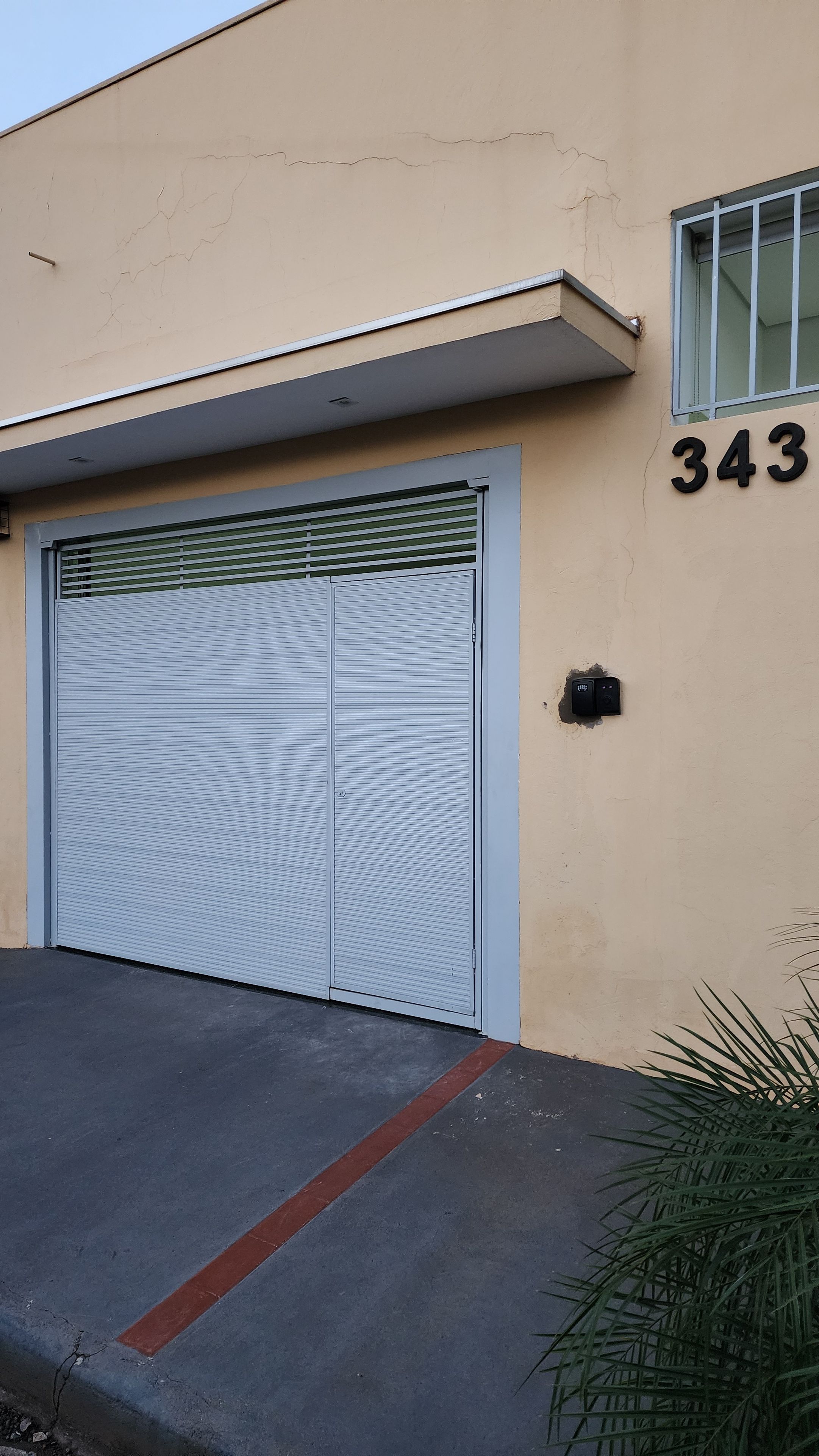 Un bâtiment avec une porte de garage fermée, une fenêtre grillagée et le numéro 343 peint sur le mur.