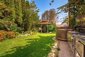 A garden with a gazebo, a barbecue area, and a variety of plants and flowers. - Jana's Garden House With Hot Tub (Kamnik)