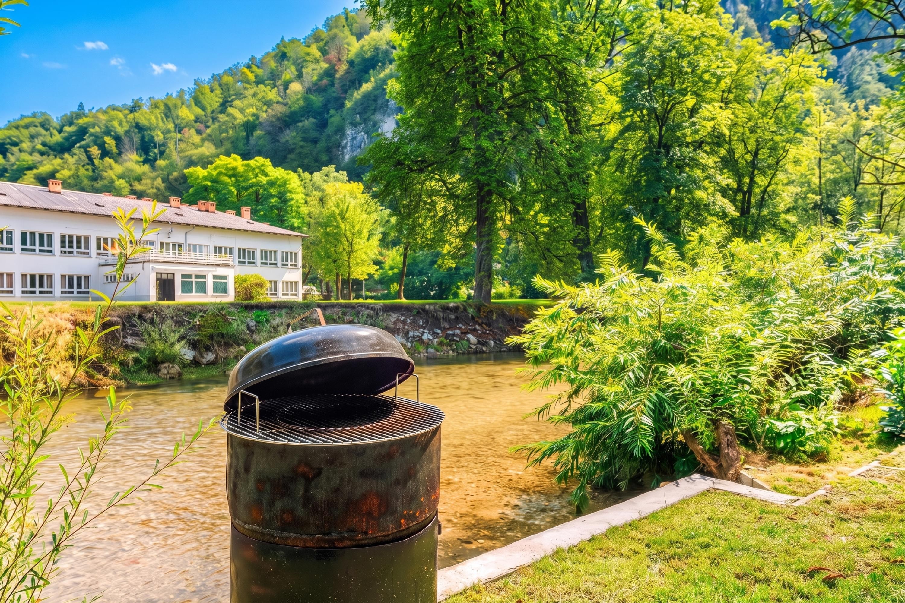 A barbecue grill in a garden with a river and a house in the background.