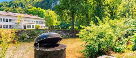 Una parrilla de barbacoa en un jardín con un río y una casa al fondo.