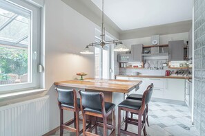 A modern kitchen with a central island, pendant lighting, and a view of greenery outside. - Jana's Garden House With Hot Tub (Kamnik)