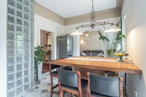 A dining area with a wooden table, two chairs, a chandelier, and a large window with a view. - Jana's Garden House With Hot Tub (Kamnik)
