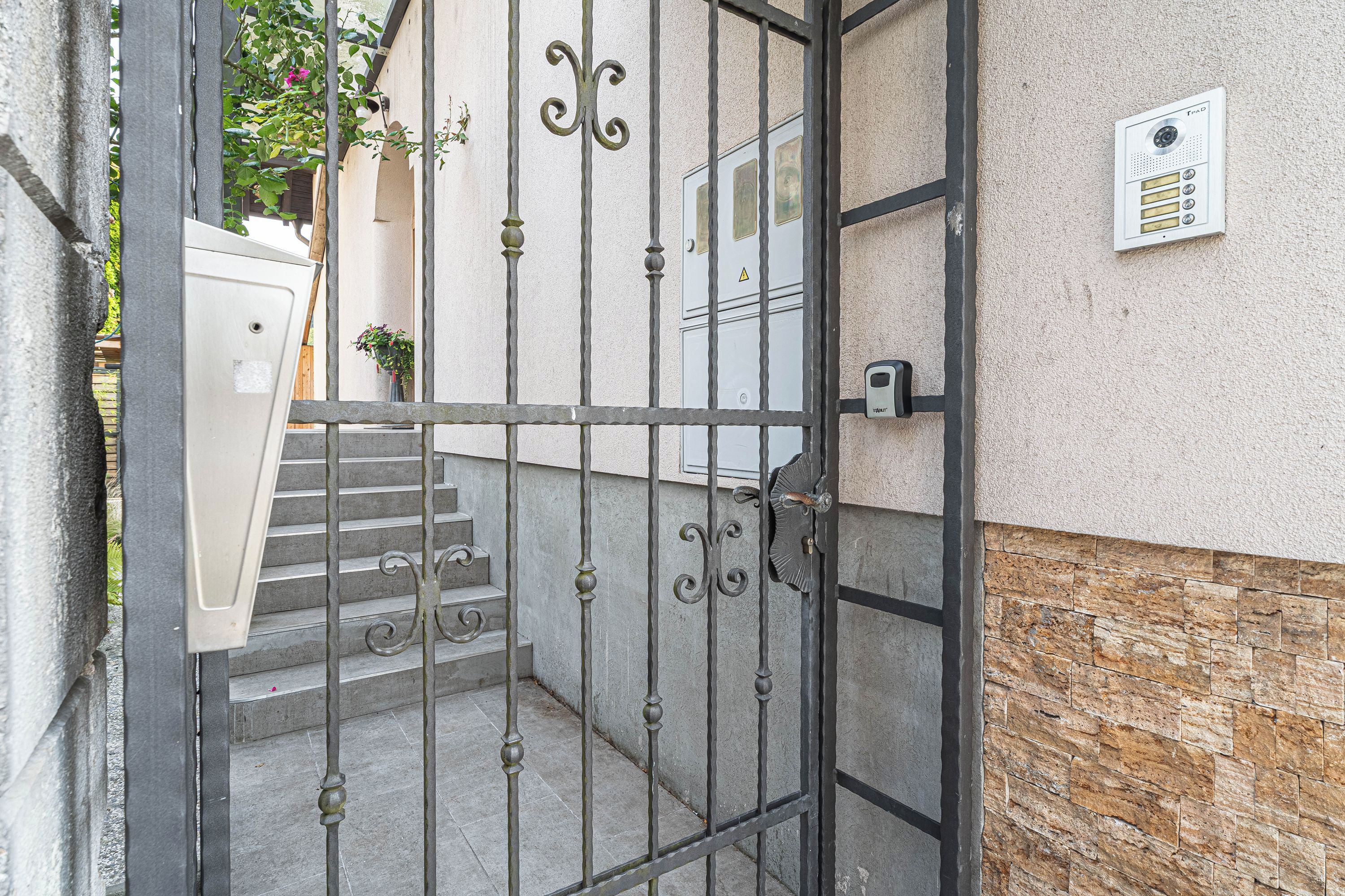 A gated entrance with a metal gate, a staircase leading to a door, and a wall-mounted intercom system.