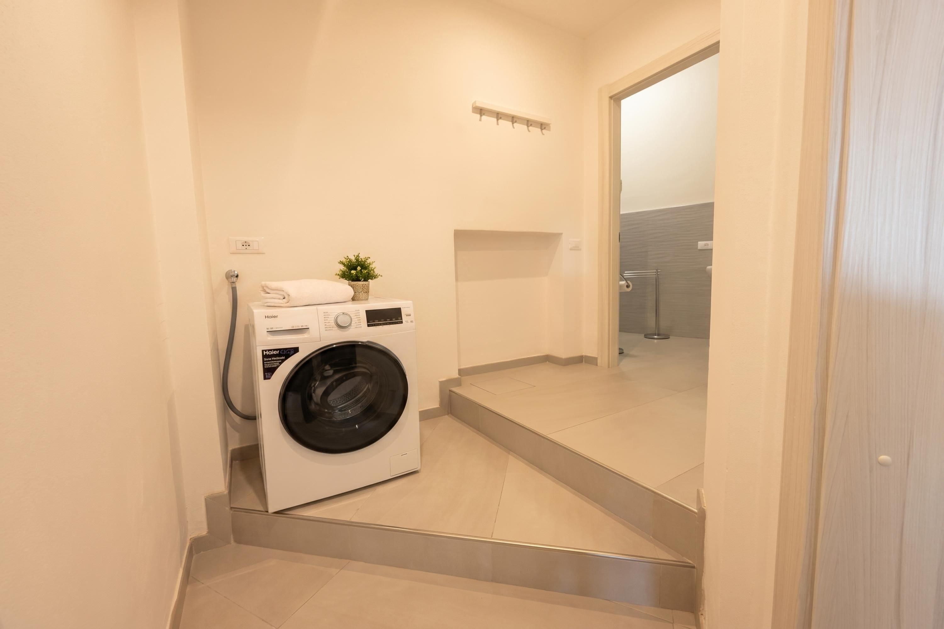 A compact laundry room with a front-loading washer and dryer, a small potted plant, and a towel on the dryer.