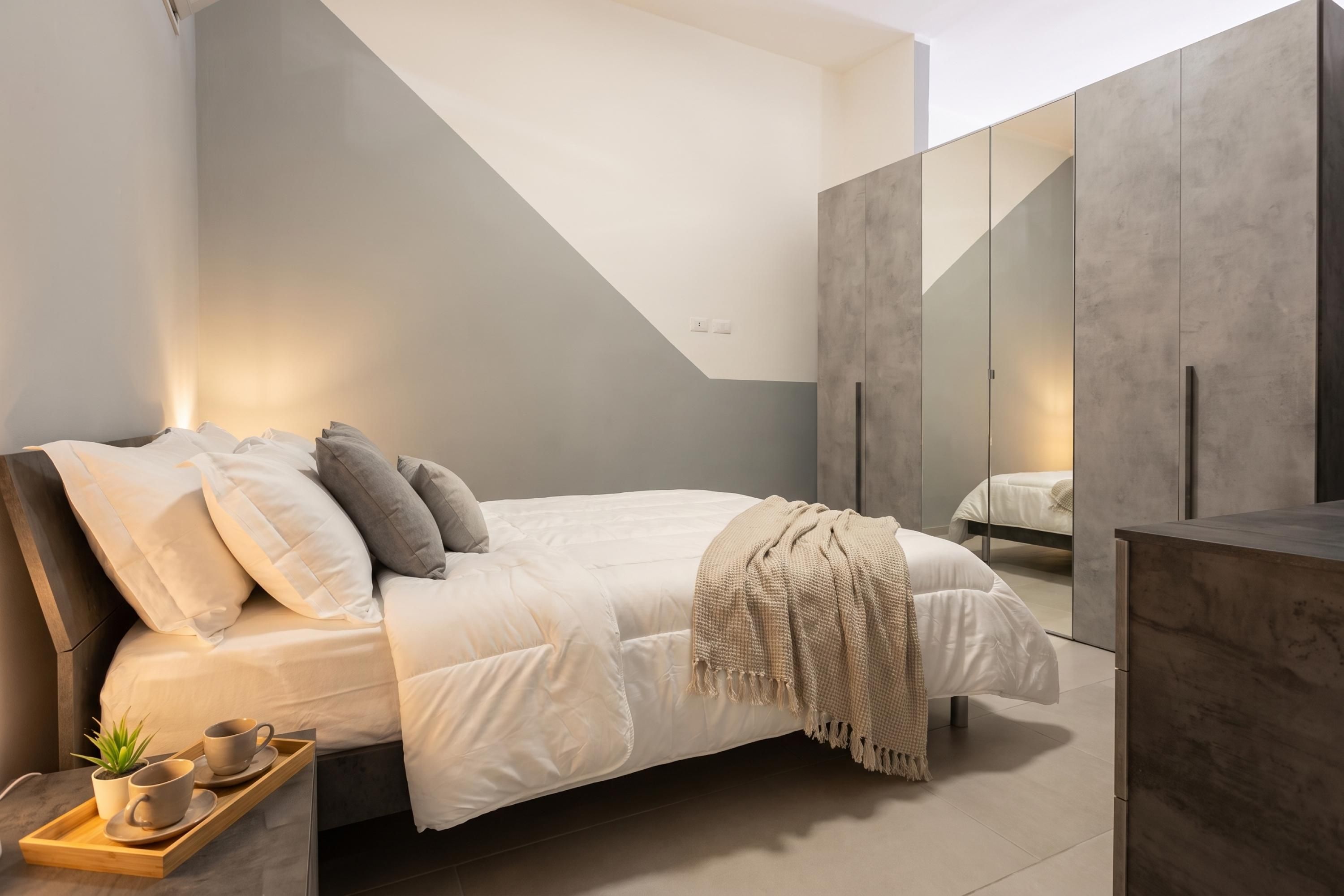 A modern bedroom with a bed, bedside tables, a mirror, and a wardrobe.