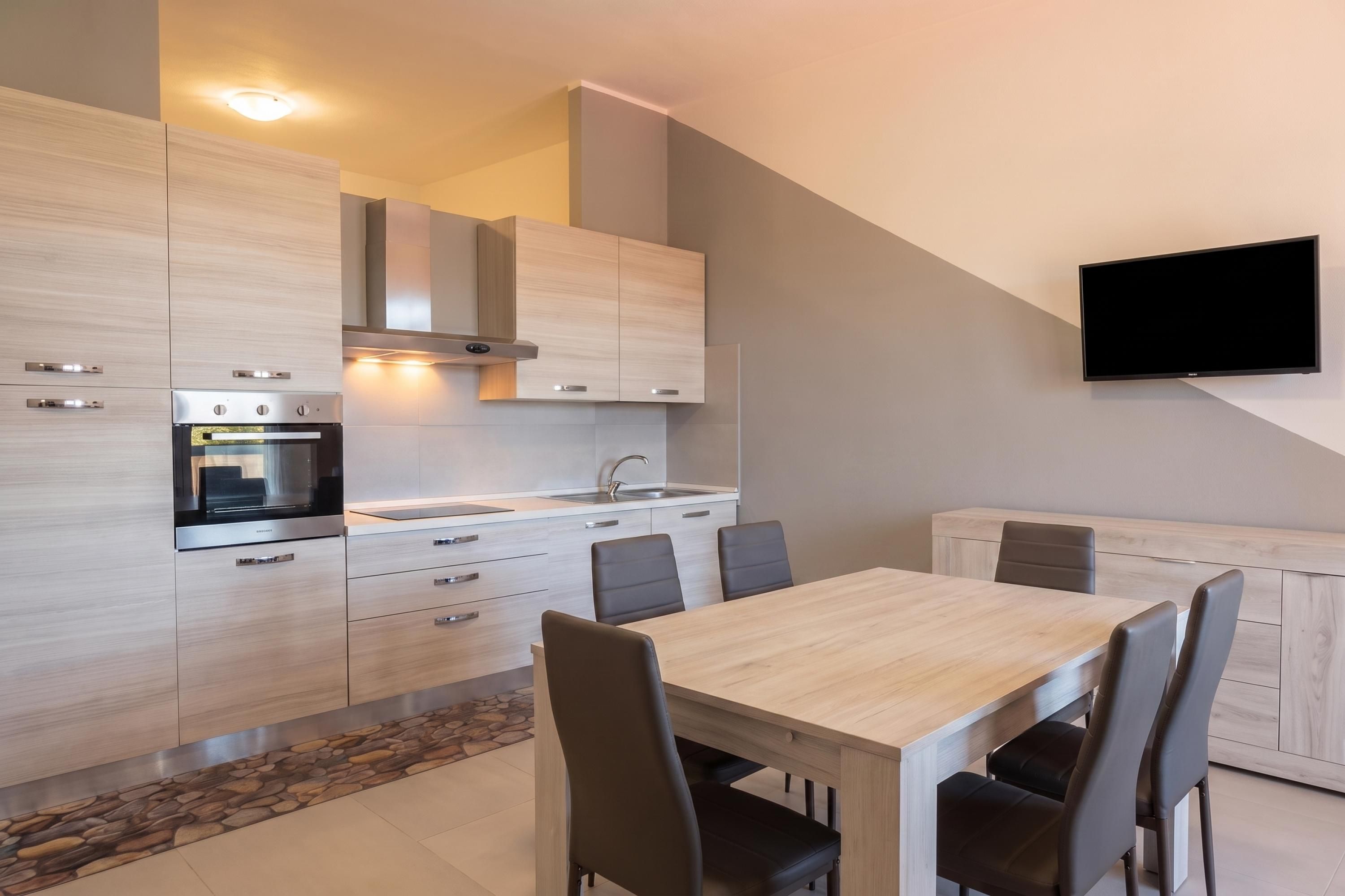 Una cocina moderna con electrodomésticos integrados, un comedor con mesa y sillas, y un televisor de pantalla plana montado en la pared.