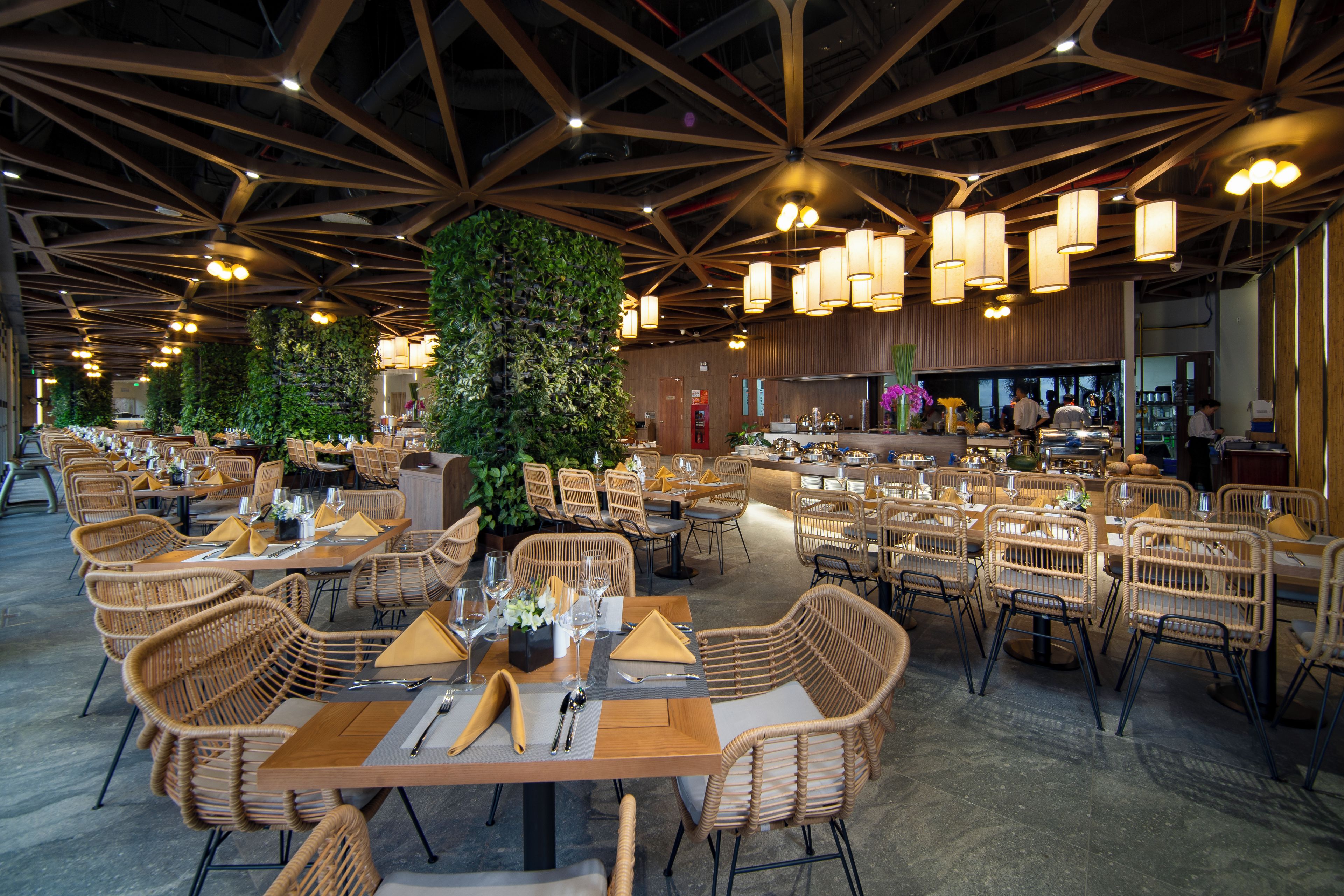 A spacious restaurant with high ceilings, multiple dining tables, and wicker chairs.