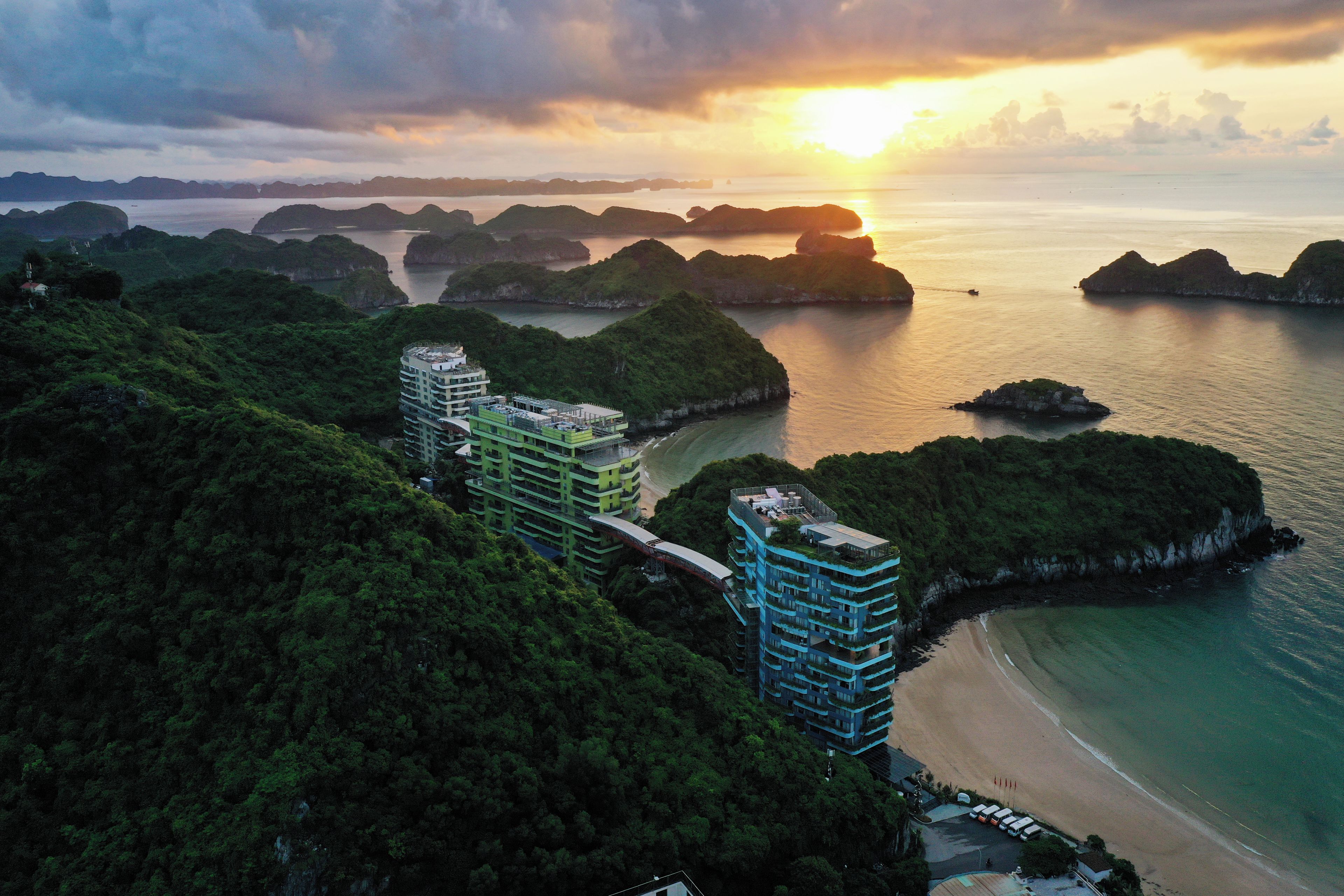 A coastal hotel with multiple buildings, a beach, and surrounding islands.