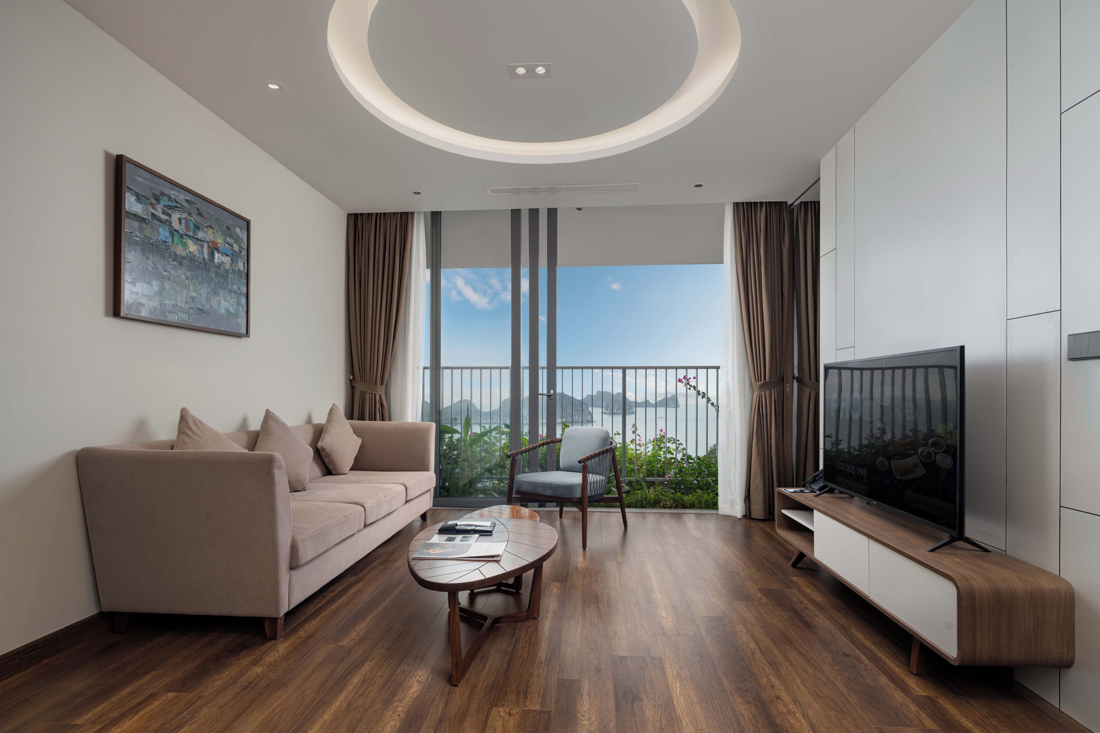 A modern living room with a sofa, a chair, a coffee table, a TV, and a balcony with a view.