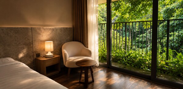 A hotel room with a bed, a chair, a nightstand with a lamp, and a large window with a view of greenery.