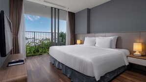 A modern hotel room with a large bed, two bedside lamps, a TV, and a balcony with a view of the city. - Cat Ba Sea & Sand Resort (Cat Hai)