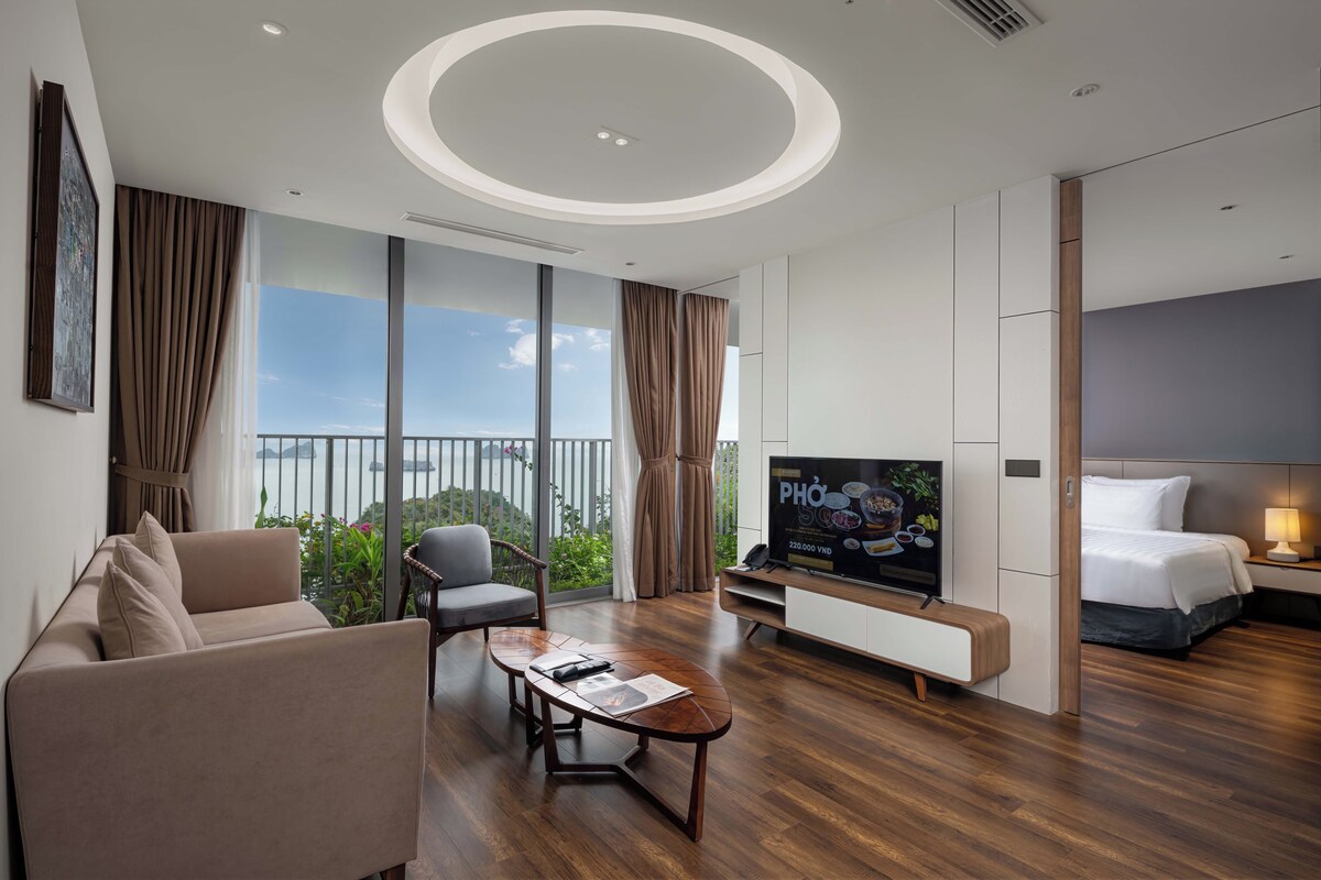 A modern hotel room with a large bed, a TV, a sofa, and a balcony with a view.