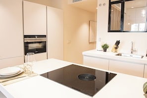Eine moderne Küche mit integriertem Induktionskochfeld, einem Edelstahl-Spülbecken und einer Arbeitsplatte mit einem Glas Wasser und Besteck.